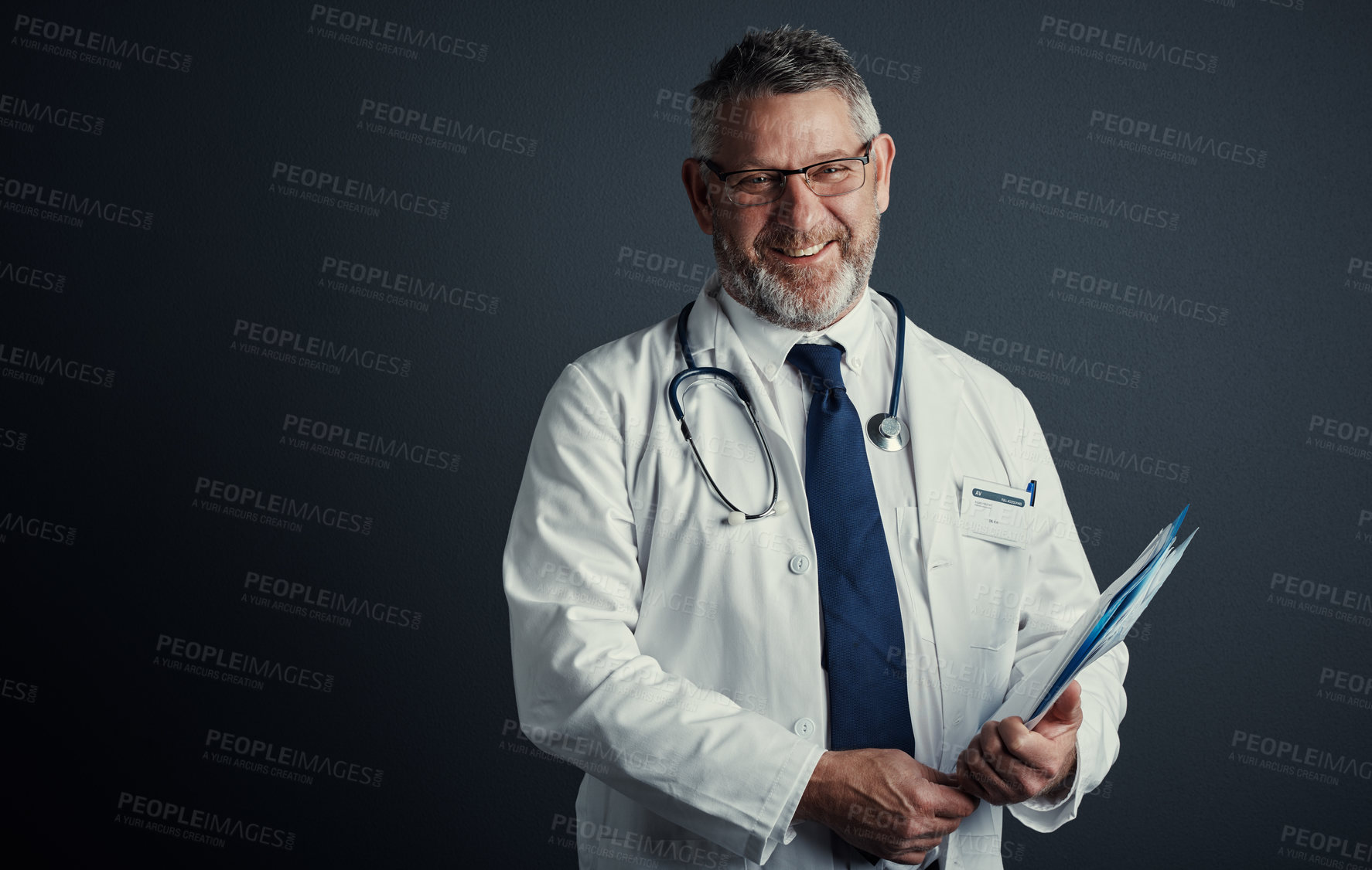 Buy stock photo Studio shot of a handsome mature male doctor holding medical records while standing against a dark background