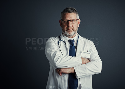 Buy stock photo Studio portrait of a handsome mature male doctor standing with his arms folded against a dark background