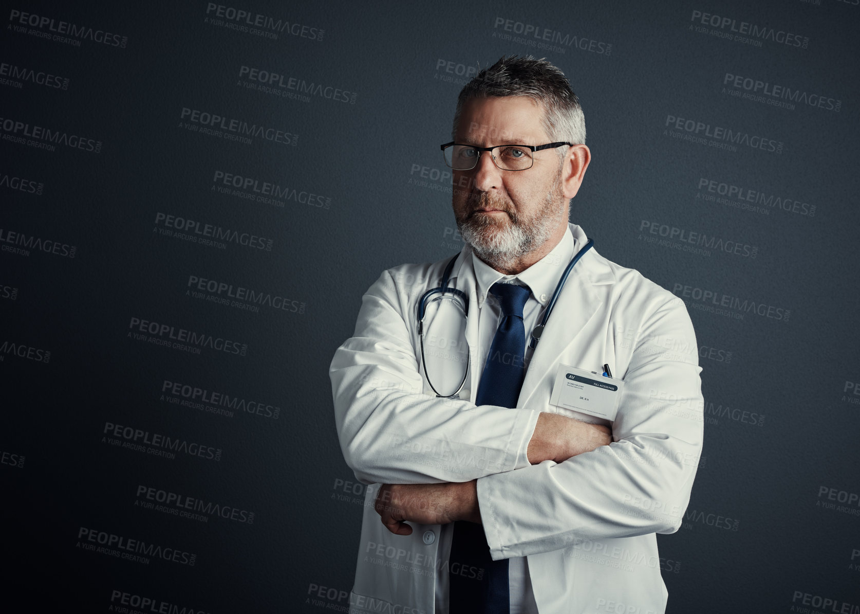 Buy stock photo Studio portrait of a handsome mature male doctor standing with his arms folded against a dark background