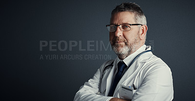 Buy stock photo Studio portrait of a handsome mature male doctor standing with his arms folded against a dark background