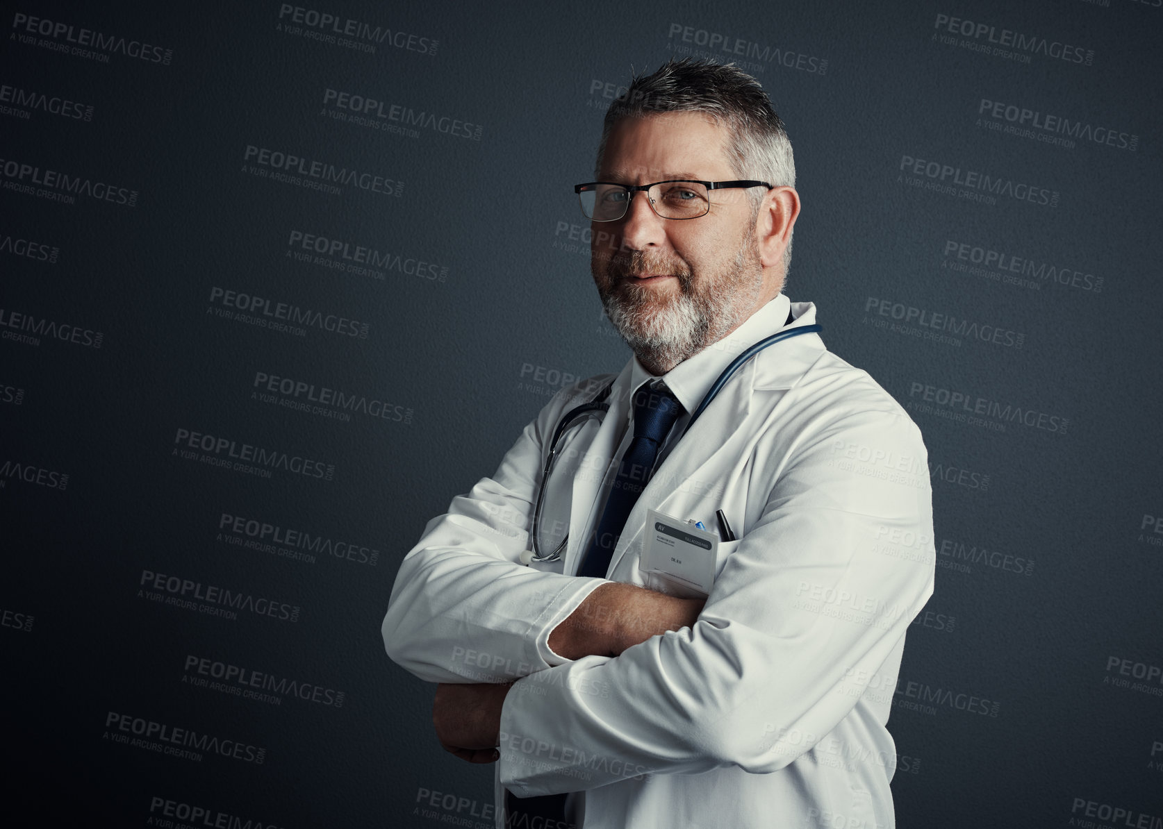 Buy stock photo Studio portrait of a handsome mature male doctor standing with his arms folded against a dark background