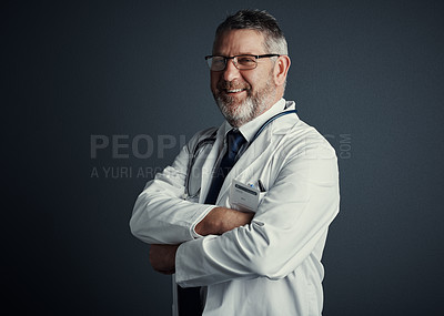 Buy stock photo Studio portrait of a handsome mature male doctor standing with his arms folded against a dark background