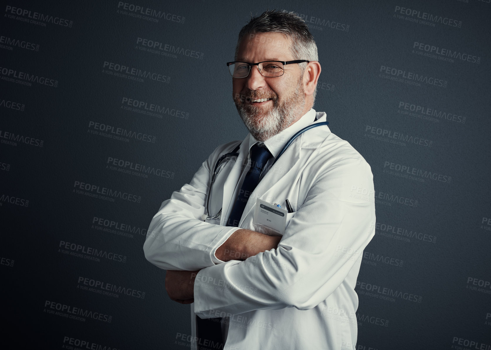 Buy stock photo Studio portrait of a handsome mature male doctor standing with his arms folded against a dark background