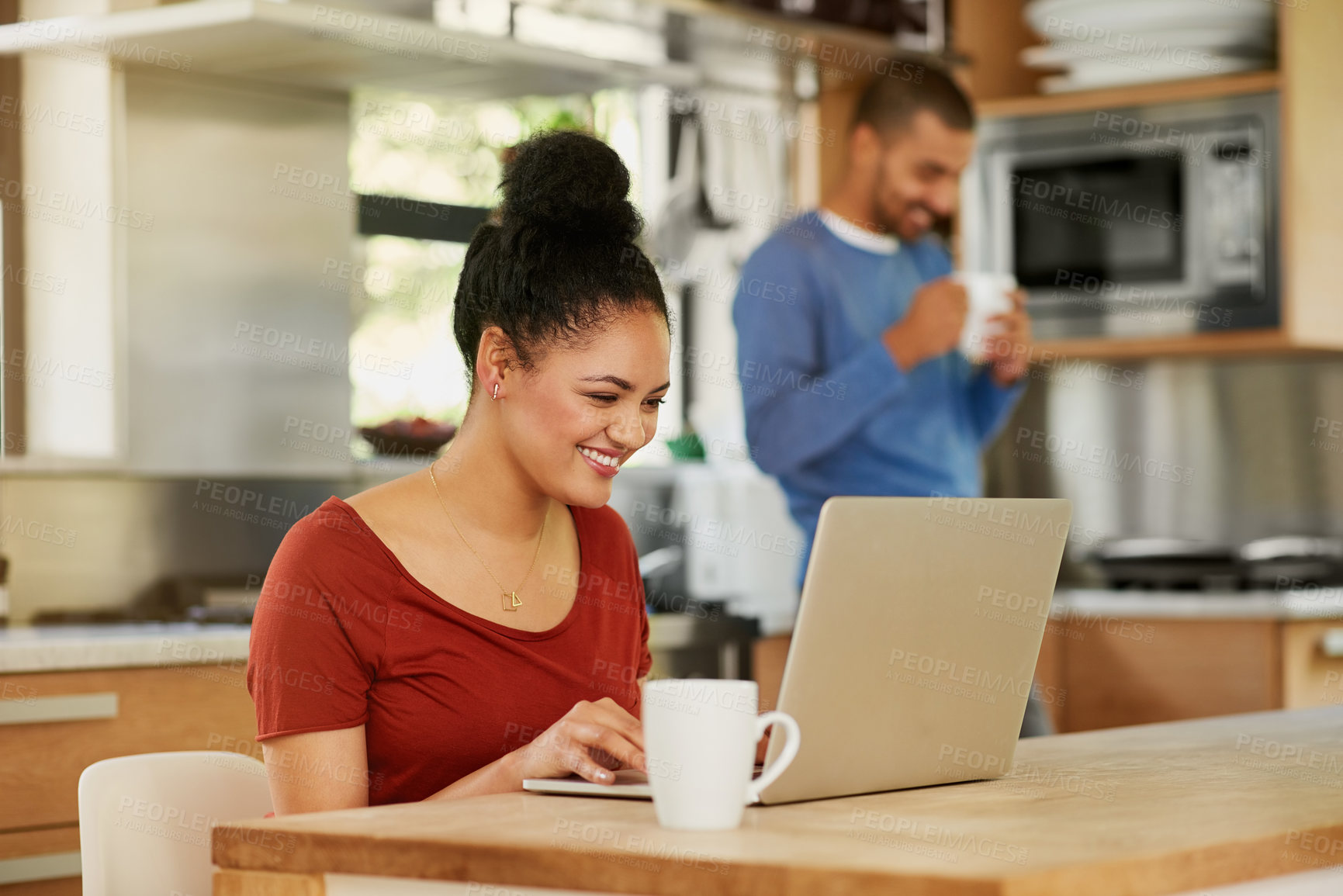 Buy stock photo Shot of a happy young woman using a laptop at home with her husband in the background