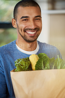 Buy stock photo Portrait of a happy young man holding a bag full of healthy vegetables at home