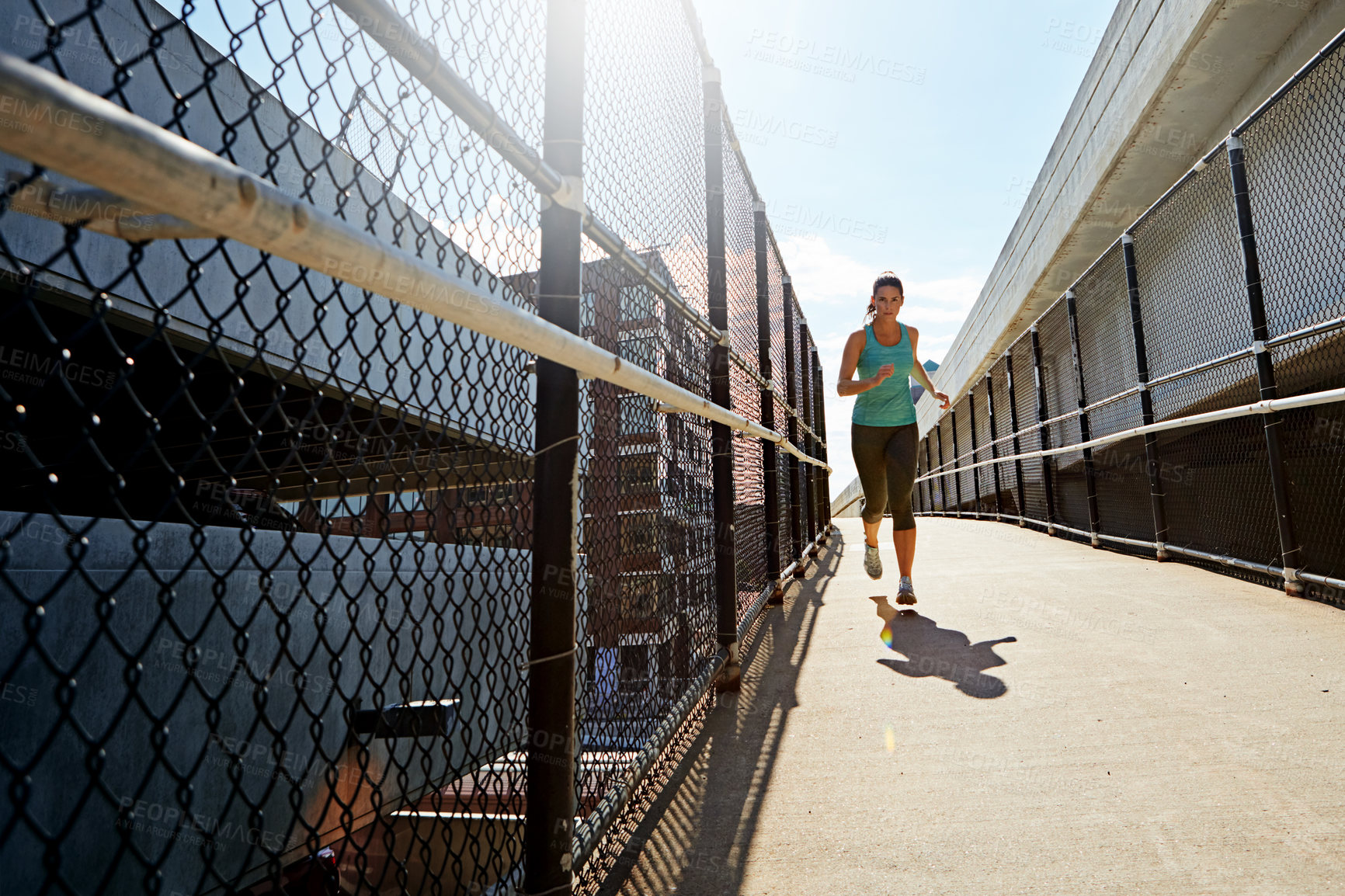 Buy stock photo Shot of a sporty young woman running on a footbridge