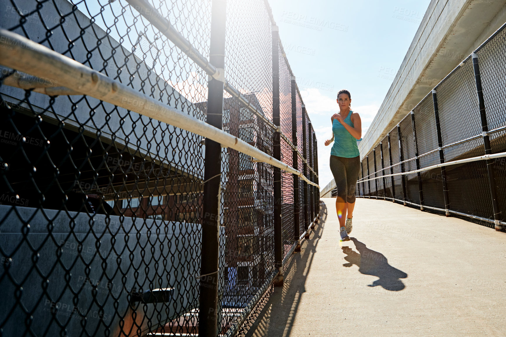 Buy stock photo Shot of a sporty young woman running on a footbridge