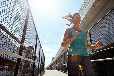 Buy stock photo Shot of a sporty young woman running on a footbridge