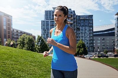 Buy stock photo Shot of a young woman listening to music while out running