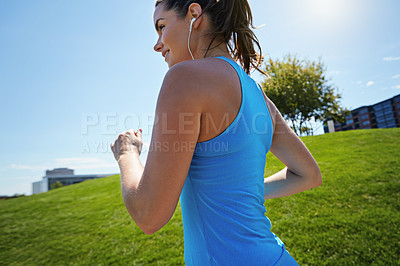 Buy stock photo Shot of a young woman listening to music while out running