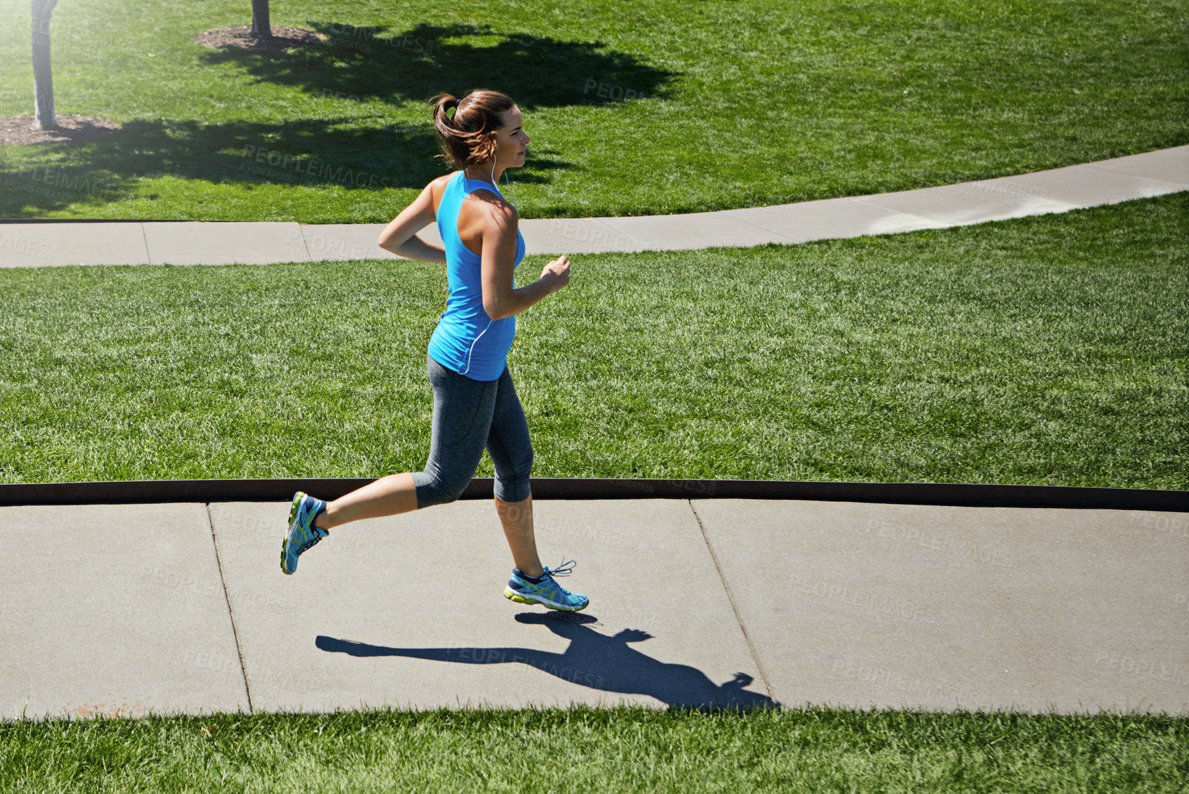 Buy stock photo Shot of a young woman listening to music while out running