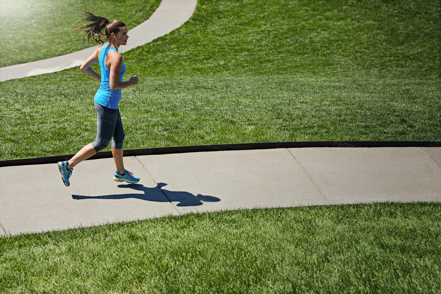 Buy stock photo Shot of a young woman listening to music while out running