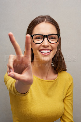 Buy stock photo Studio portrait of an attractive young woman giving you the peace sign while posing against a grey background