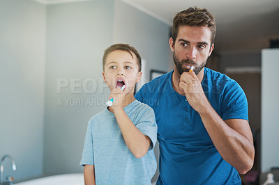 Buy stock photo Cropped shot of a handsome young man and his son brushing their teeth in the bathroom