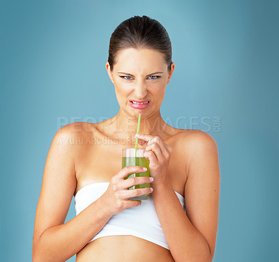 Buy stock photo Studio portrait of a beautiful young woman drinking a healthy green beverage and looking disgusted against a blue background