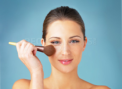 Buy stock photo Studio portrait of a beautiful young woman using a makeup brush on her face against a blue background