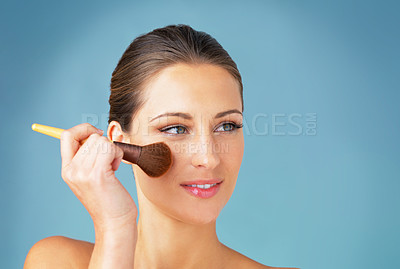 Buy stock photo Studio shot of a beautiful young woman using a makeup brush on her face against a blue background