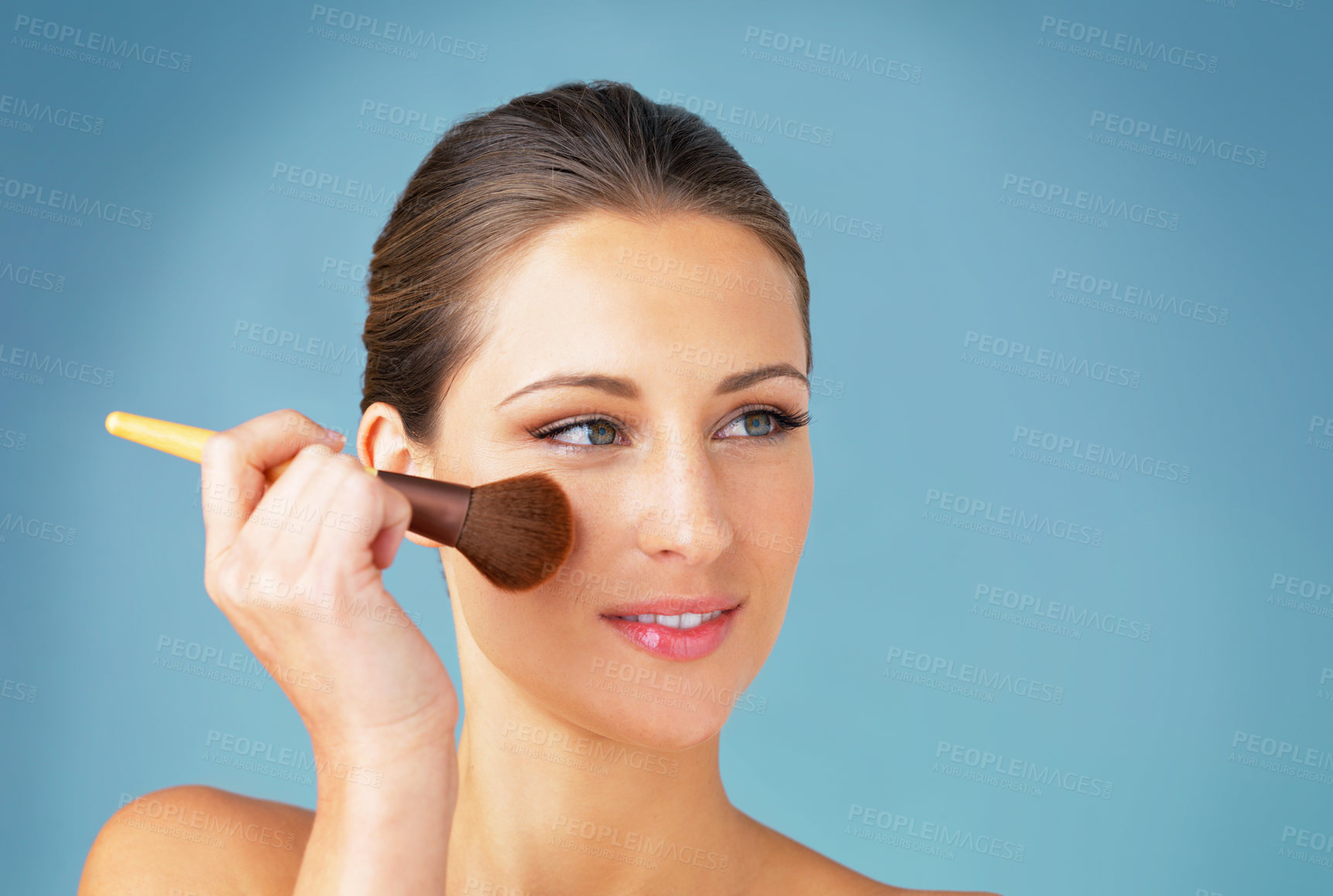 Buy stock photo Woman, makeup brush and powder on cheek in studio for natural glow, blush cosmetics and makeover. Female person, face and tool for foundation application, shine and facial beauty by blue background