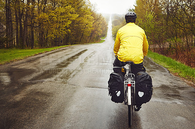 Buy stock photo Rearview shot of a male cyclist enjoying a bike ride on a wet winter's morning