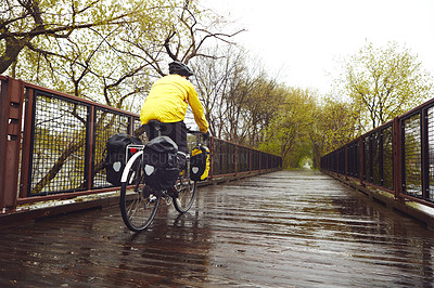 Buy stock photo Rearview shot of a male cyclist enjoying a bike ride on a wet winter's morning