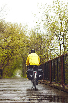 Buy stock photo Rearview shot of a male cyclist enjoying a bike ride on a wet winter's morning