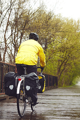 Buy stock photo Rearview shot of a male cyclist enjoying a bike ride on a wet winter's morning