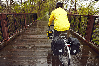 Buy stock photo Rearview shot of a male cyclist enjoying a bike ride on a wet winter's morning