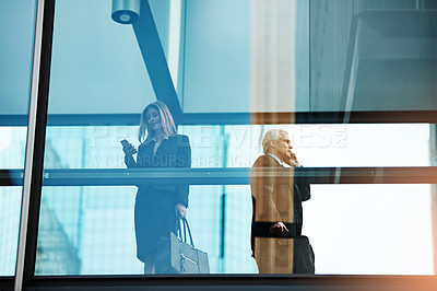 Buy stock photo Shot of businesspeople using their mobile phones in a modern glass office