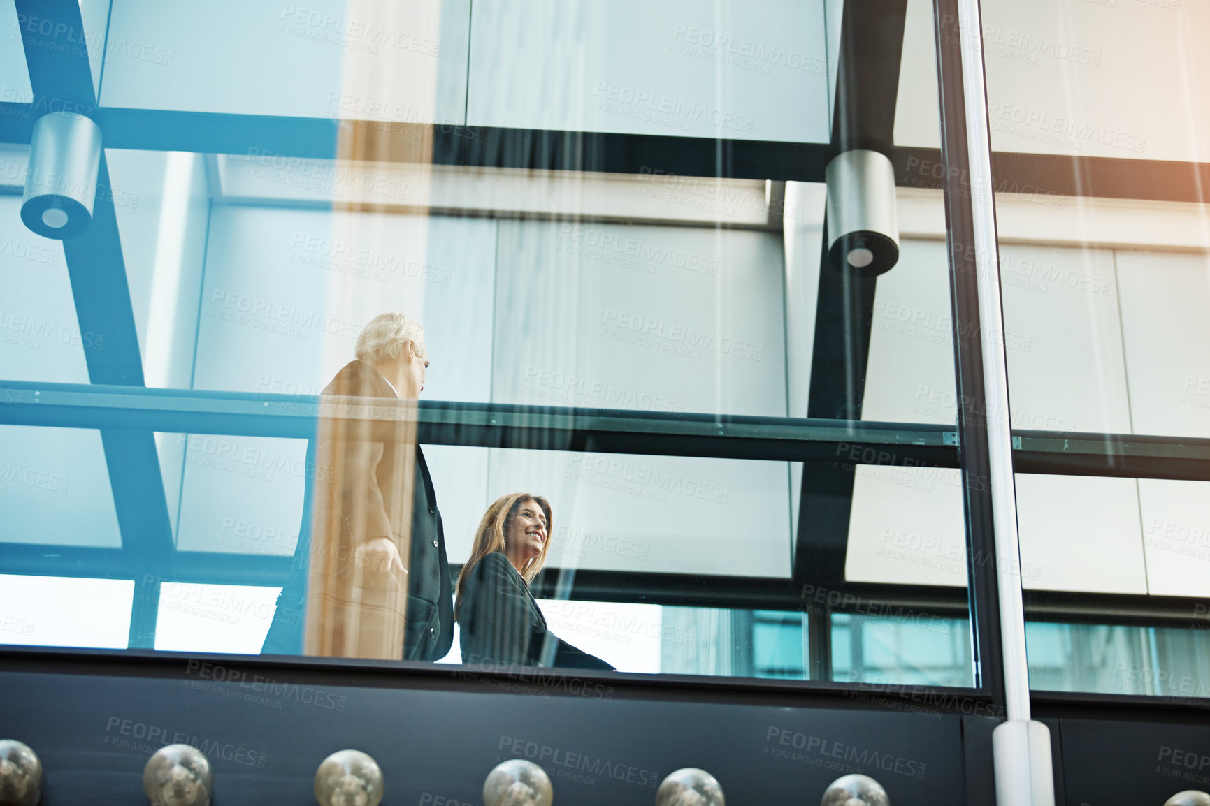 Buy stock photo Walking, glass and business people by window for commute, journey and discussion for planning. Corporate, team and low angle of man and woman in hallway for meeting, collaboration or networking