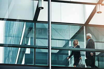 Buy stock photo Shot of a businessman and businesswoman walking and talking in a modern glass office