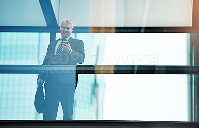 Buy stock photo Shot of a mature businessman using a mobile phone in a modern glass office