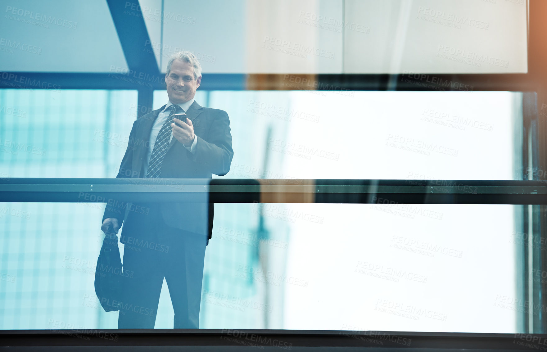 Buy stock photo Shot of a mature businessman using a mobile phone in a modern glass office