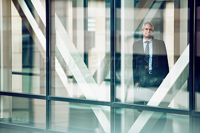 Buy stock photo Portrait of a mature businessman looking out of the window in a modern glass office
