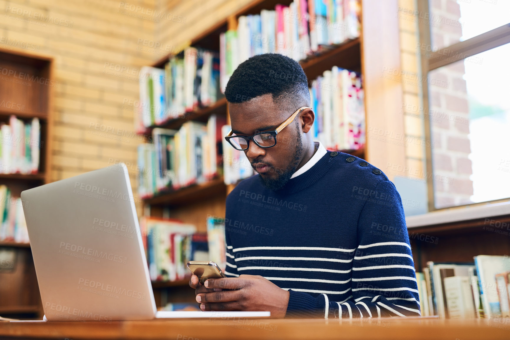 Buy stock photo Phone, typing and black man with laptop in library at university for education, communication or online chat. Computer, smartphone and college student on mobile app for schedule, research or project