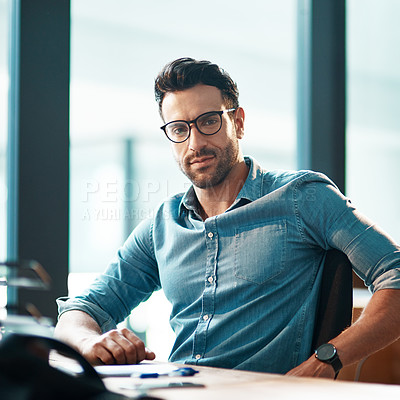 Buy stock photo Young, confident and professional business man wearing glasses, sitting at his desk and working in a modern office portrait. A casual and serious corporate male in the finance department