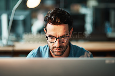 Buy stock photo Serious business man working at computer late in the office at night to finish reports, articles or code. Focused and young male IT worker wearing glasses late in the evening for deadline