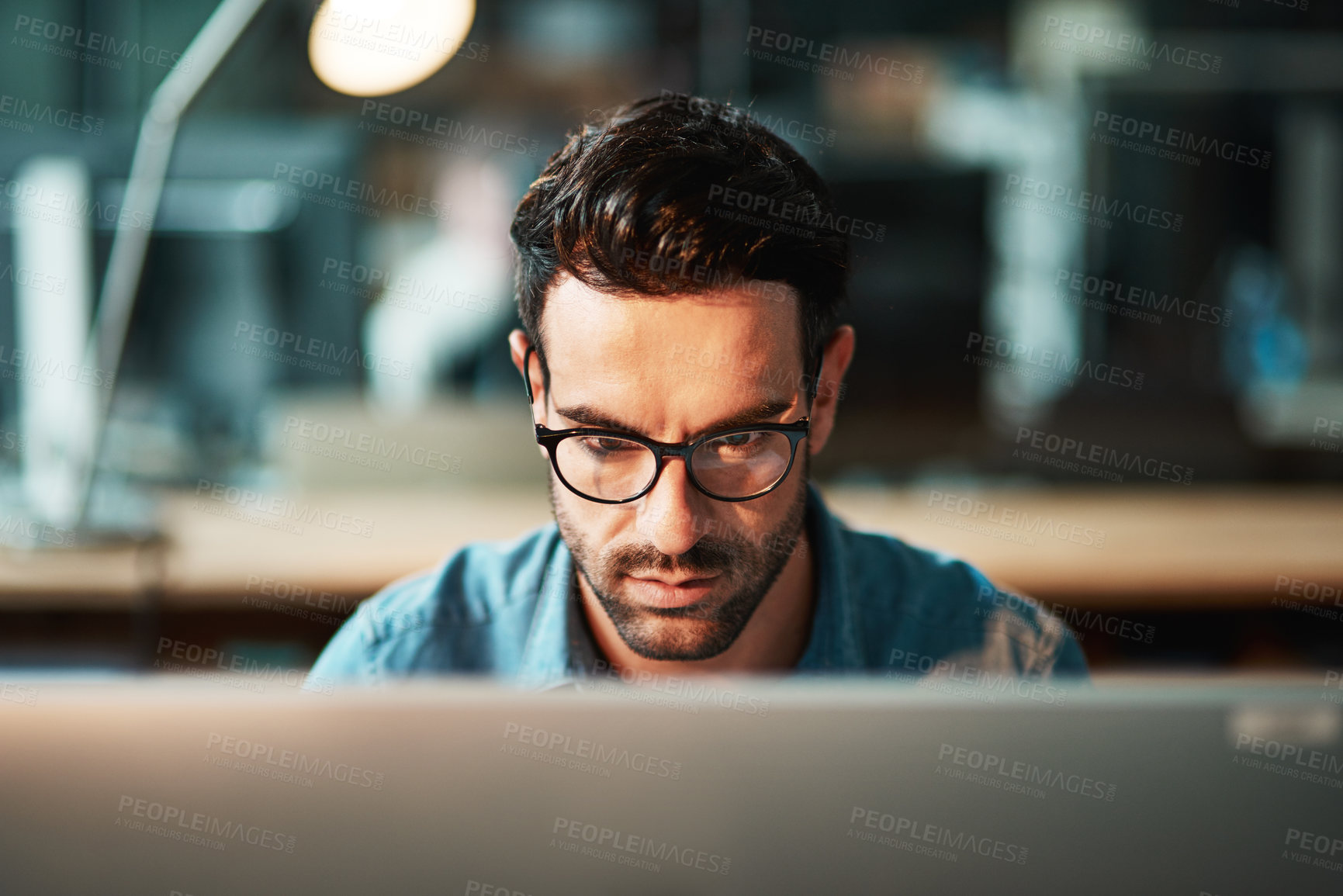 Buy stock photo Serious business man working at computer late in the office at night to finish reports, articles or code. Focused and young male IT worker wearing glasses late in the evening for deadline