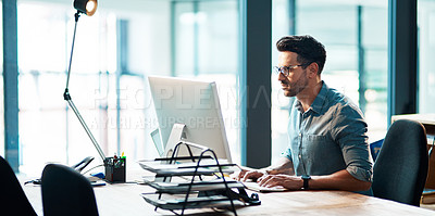 Buy stock photo Shot of a focused young businessman using a computer at his desk in a modern office