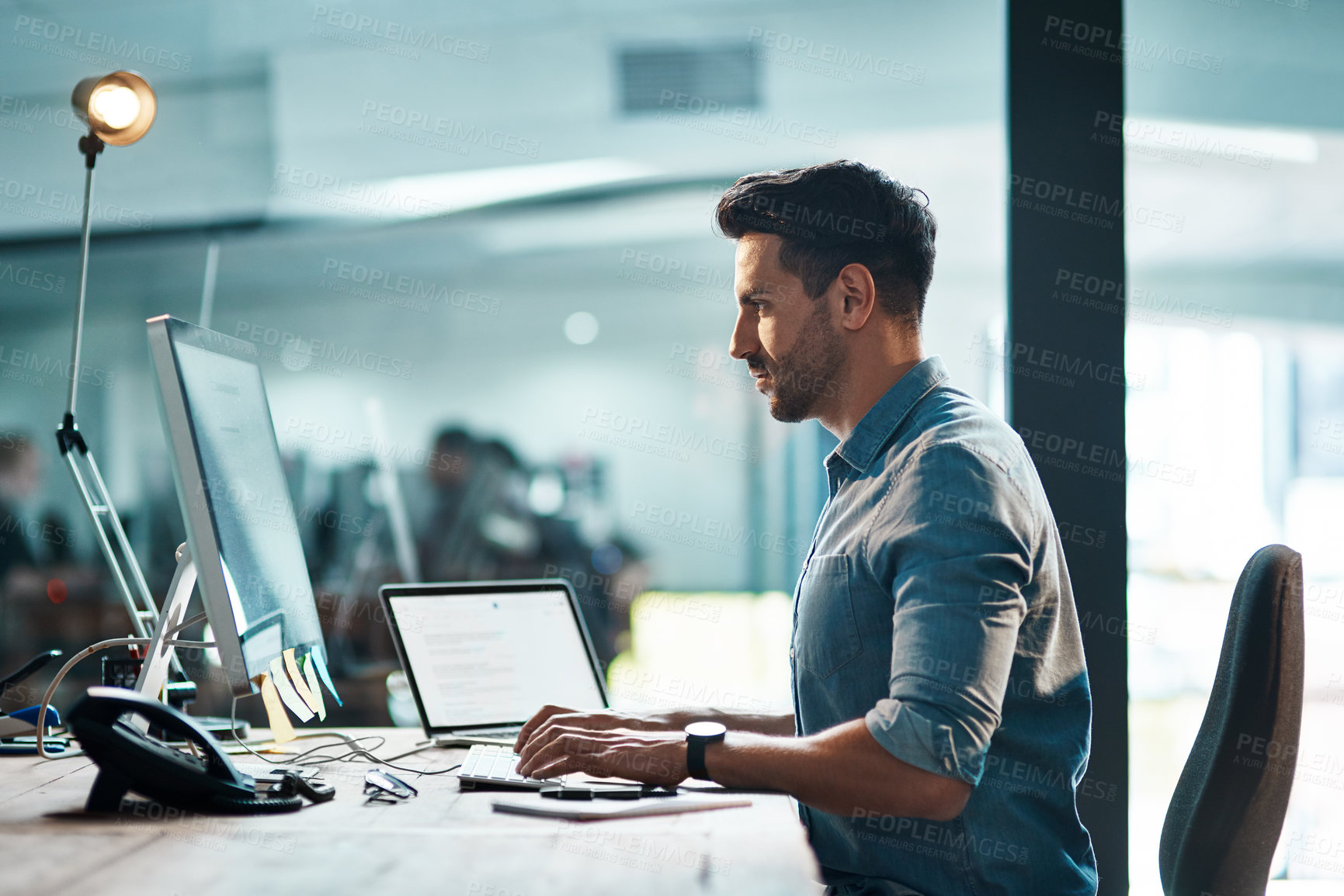 Buy stock photo Shot of a young businessman using a computer at his desk in a modern office