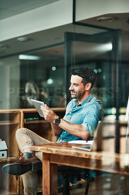 Buy stock photo Confident, relaxed and carefree entrepreneur, creative designer or project manager browsing on a tablet and sitting in his office at work. Young man managing online orders with wireless technology