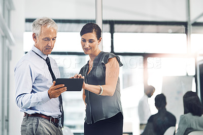 Buy stock photo Cropped shot of two corporate businesspeople looking at a tablet while standing in the office