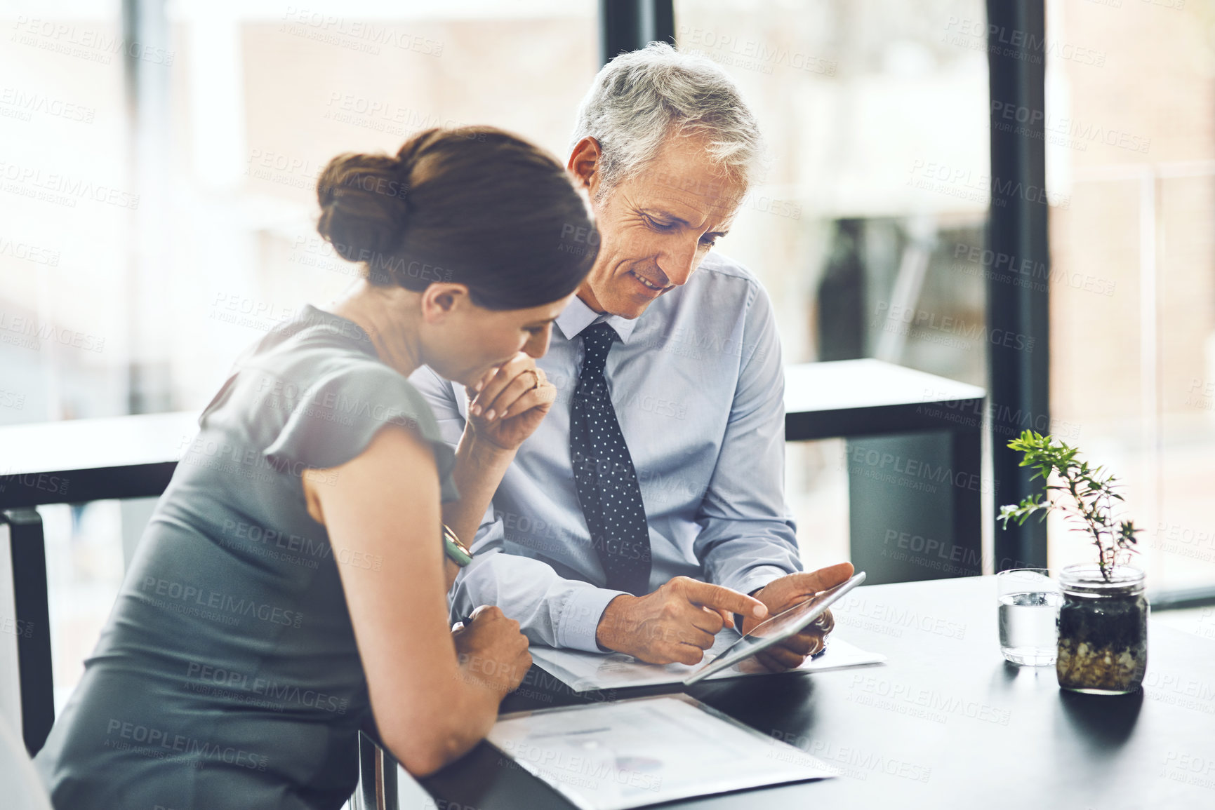 Buy stock photo Cropped shot of two corporate businesspeople looking at a tablet while sitting in the office