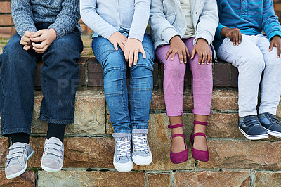 Buy stock photo Shot of a group of unrecognizable elementary school kids sitting on a brick wall outside