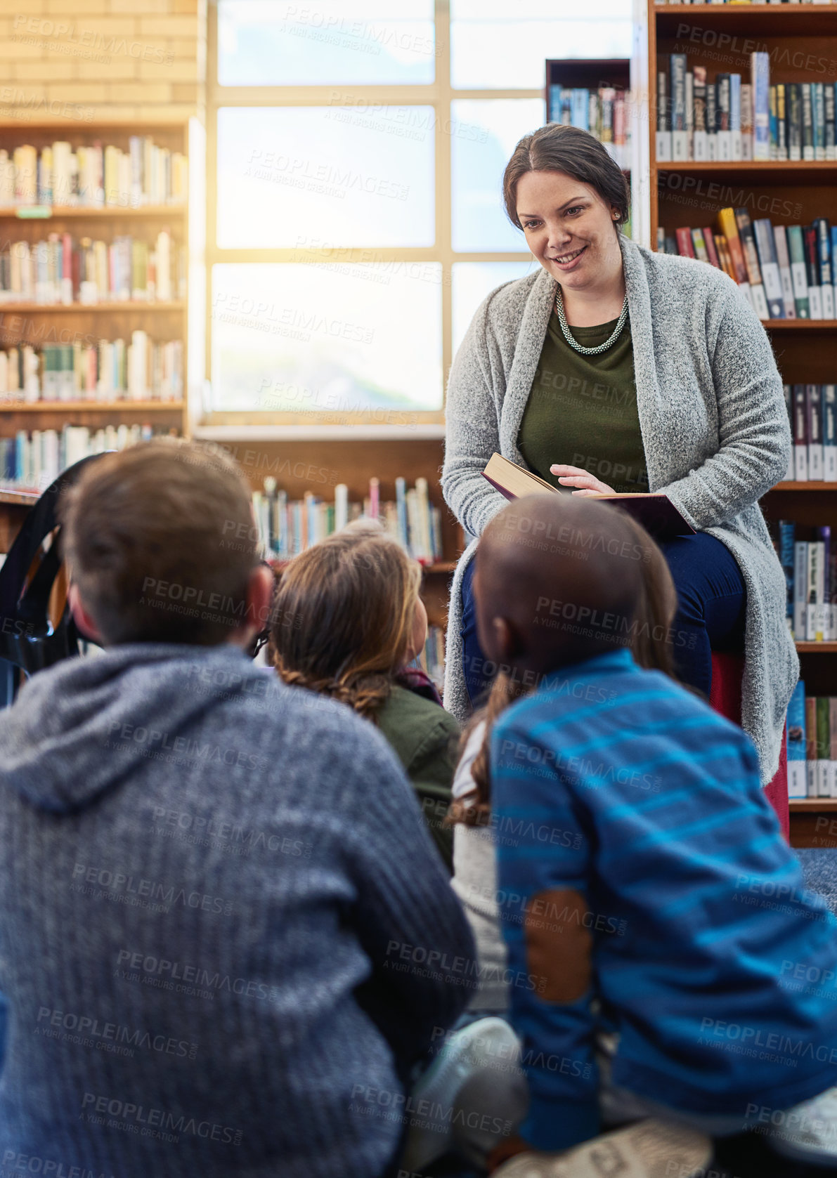 Buy stock photo Shot of a teacher reading to a group of elementary school kids in the library