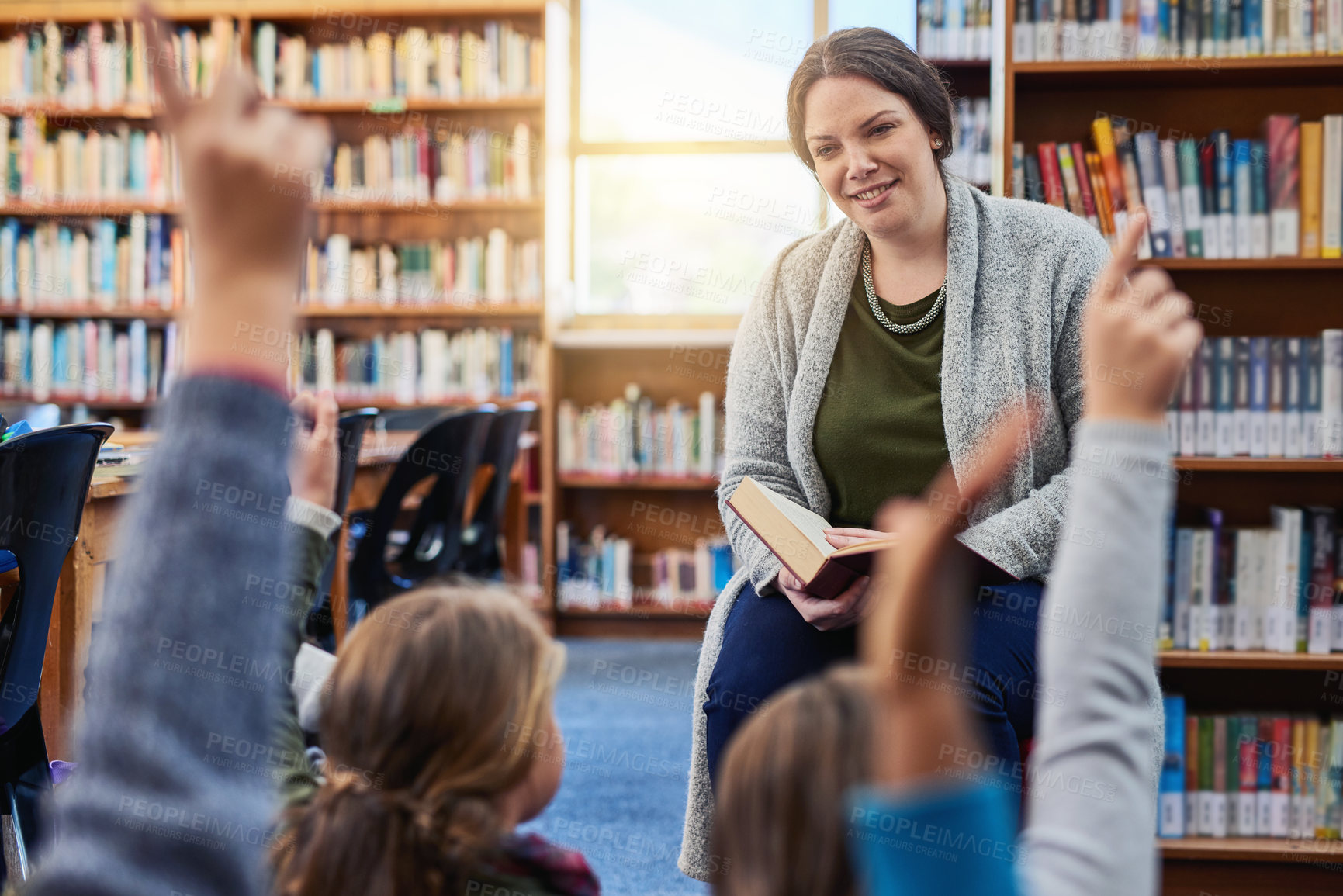 Buy stock photo Shot of a group of elementary school kids raising their hands to their teacher in the library