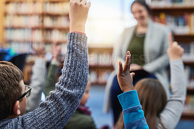 Buy stock photo Shot of a group of elementary school kids raising their hands to their teacher in the library