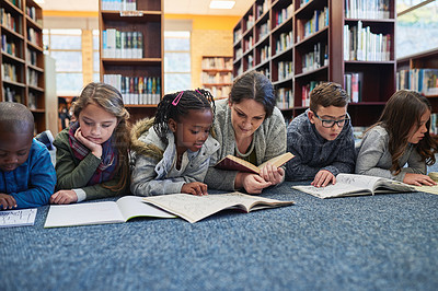 Buy stock photo Education, teacher with children in library and lying on the floor of elementary school. Studying or knowledge with books, diversity and young students with woman reading textbook or notebook.