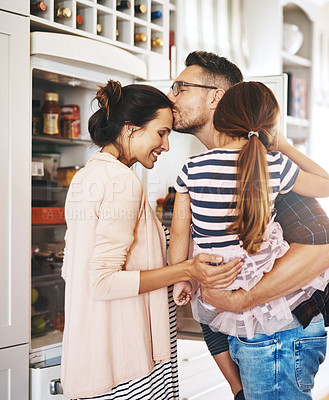 Buy stock photo Shot of a husband lovingly kissing his pregnant wife in the kitchen while holding his daughter