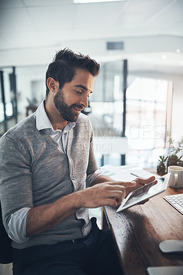 Buy stock photo Shot of a young businessman working on a digital tablet in an office