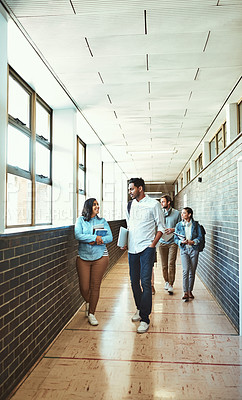 Buy stock photo Full length shot of a group of university students walking through a campus corridor